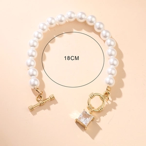 Elegant pearl bracelet with golden OT clasp and square zircon pendant on beige background