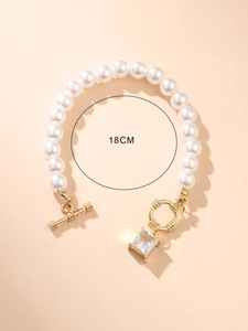 Detail of elegant pearl bracelet with golden OT clasp and clear square gemstone charm