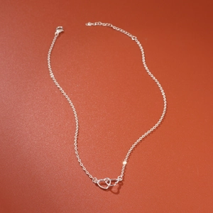 Minimalist silver interlocking heart necklace with adjustable chain on textured background