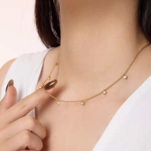 Detailed close-up of a delicate 18K gold beaded necklace with five clear zircon pendants