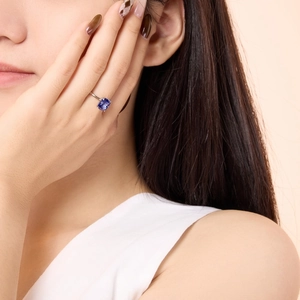 Close-up of a cushion-cut deep blue gemstone ring on model finger in silver setting