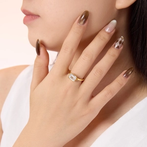 Close-up of emerald cut clear gemstone ring on model finger with gold finish