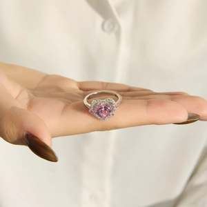 Nahaufnahme des rosa herzförmigen Zirkonrings mit weißen Steinen auf einer Hand