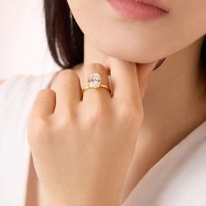 Close-up of elegant gold bezel-set oval gemstone ring on model's hand with refined detail
