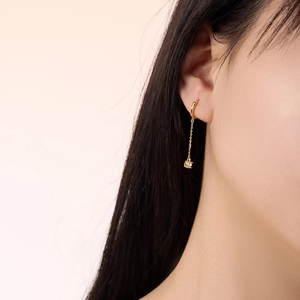 Detailed close-up of a long gold chain earring with a square crystal pendant on a model