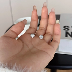 Macro detail of S925 sterling silver moissanite stud earrings held by hand for size comparison