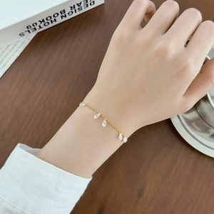 Close-up of elegant gold chain bracelet with pear-shaped crystal pendants on woman wrist