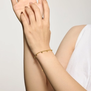 Détail d'un bracelet minimaliste à perles dorées avec pendentif cœur porté au poignet