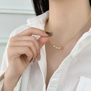 Detail of minimalist gold-plated necklace with three polished round bead pendants on model