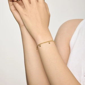 Détail d'un délicat bracelet en or avec de petits charms en forme de cœur au poignet
