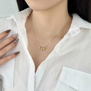 Minimalist gold necklace with three polished round beads on a fine chain worn by a model