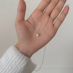 Gros plan d'un collier en argent S925 avec pendentif moissanite ovale de 1 carat en main