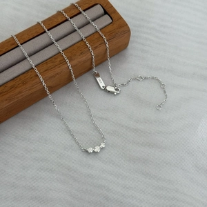 Minimalist S925 sterling silver necklace featuring three sparkling round zircons on a wooden stand