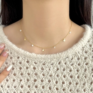 Detailed close-up of a gold star necklace with zircon stones on a beige sweater