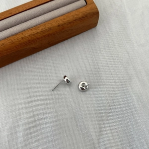 Detailed view of silver stud earrings with a single round diamond set on a grey textured fabric