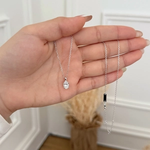 Close-up of 1.5 carat oval moissanite pendant on silver chain held by a hand