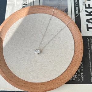 Macro shot of minimalist silver necklace with round solitaire diamond in wooden tray