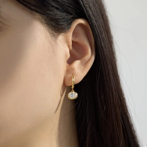 Macro side view of a model wearing a gold pendant earring with a sparkling round zircon