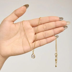 Détail d'un pendentif goutte de poire sur une chaîne en or tenue dans la main