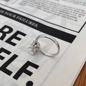 Détail d'une bague moissanite taille ovale avec entourage halo sur un magazine