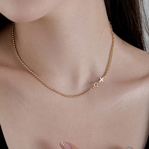 Detail of gold cross necklace with asymmetric bead chain and female symbol on collarbone
