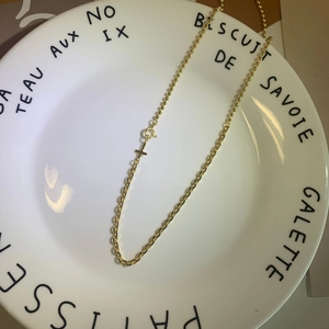 Detail of gold cross pendant on mixed bead and link chain over decorative plate