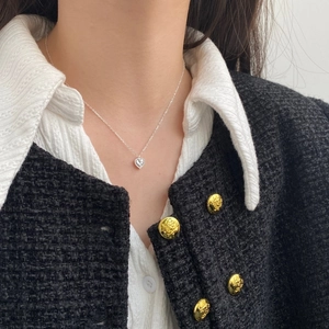 Detail view of heart-shaped zircon pendant on silver necklace worn over white shirt