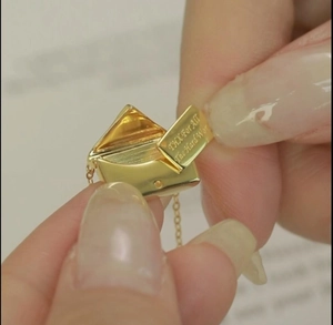 Detailed view of an open golden envelope pendant with engraved thank you message
