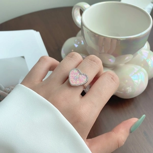Detailed view of a heart-shaped pink opal ring on a finger in a cozy setting