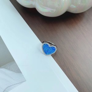 Macro shot of silver heart ring with blue opal stone and shimmering pavé halo detail