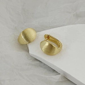 Detail view of gold textured oval hoop earrings with a brushed matte metallic finish