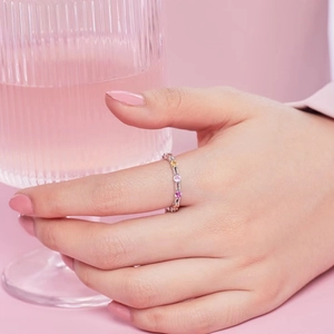 Bague en argent S925 sertie de zircons colorés sur main de femme avec fond rose doux
