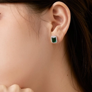 Détail de boucles d'oreilles avec pierre verte taille émeraude et serti halo sur modèle