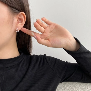Model trägt silberne Herz-Ohrringe mit Kristallen vor einem eleganten schwarzen Outfit