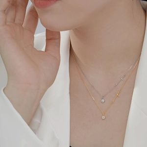 Close-up of layered silver and gold necklaces with cross charm and crystal pendant