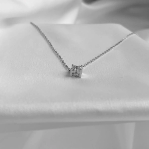 Détail du pendentif carré évidé en argent avec zircons sur un tissu de soie blanche
