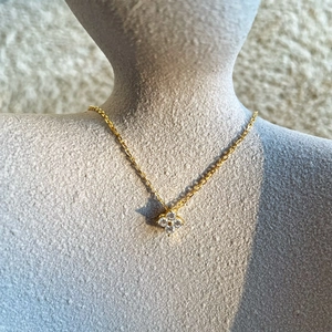 Détail d'un collier trèfle doré avec pétales en cristal sur un mannequin gris