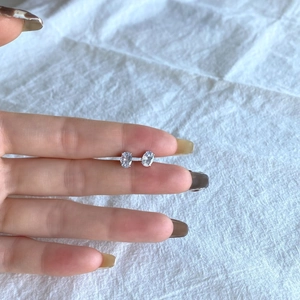 Detailed view of sterling silver oval zircon studs held by hand against linen fabric