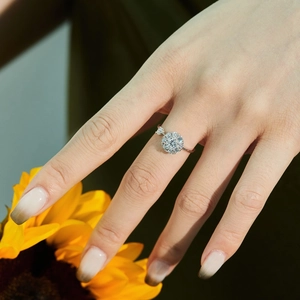 Detail eines S925 Silberrings mit Halo-Diamanten am Finger vor gelben Blumenhintergrund