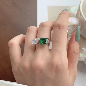 Close-up of s925 silver ring featuring emerald cut green stone and pear drop diamond on finger