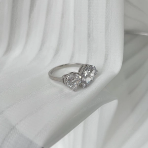 Primer plano de anillo de plata con dos gemas en forma de corazón sobre tela blanca