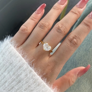 Close-up of heart-shaped zircon ring in gold finish on female hand with luxury nails