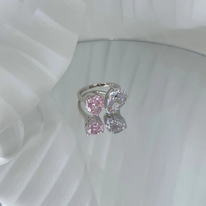 Detalle de anillo de plata S925 con corazón rosa y piedra de pera sobre superficie espejo
