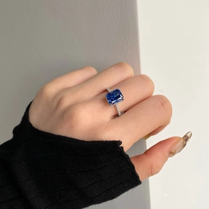 Detailed view of rectangle cut blue sapphire gemstone ring worn on finger with micro pavé