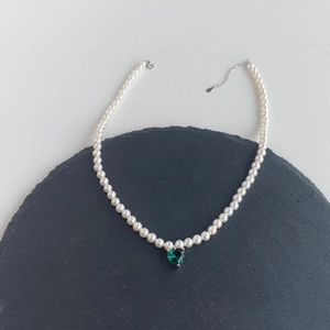 Macro detail of a pearl necklace with a green heart-shaped gemstone and lobster clasp