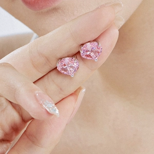 Macro shot of S925 sterling silver heart-shaped pink stud earrings held by fingers