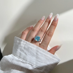 Macro detail of sky blue emerald-cut stone ring with triangle side diamonds on hand