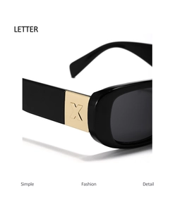 Detail of black sunglasses frame with gold metal hinge piece featuring letter X engraving