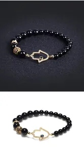 Close-up of golden Hamsa hand charm with blue evil eye and pavé crystals on black bead bracelet