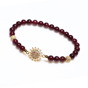 Bracelet en perles de grenat rouge avec pendentif fleur dorée et zircons sur fond blanc
